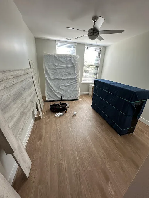 Bagged mattress, disassembled bed frame and blanket-wrapped furniture in a bedroom