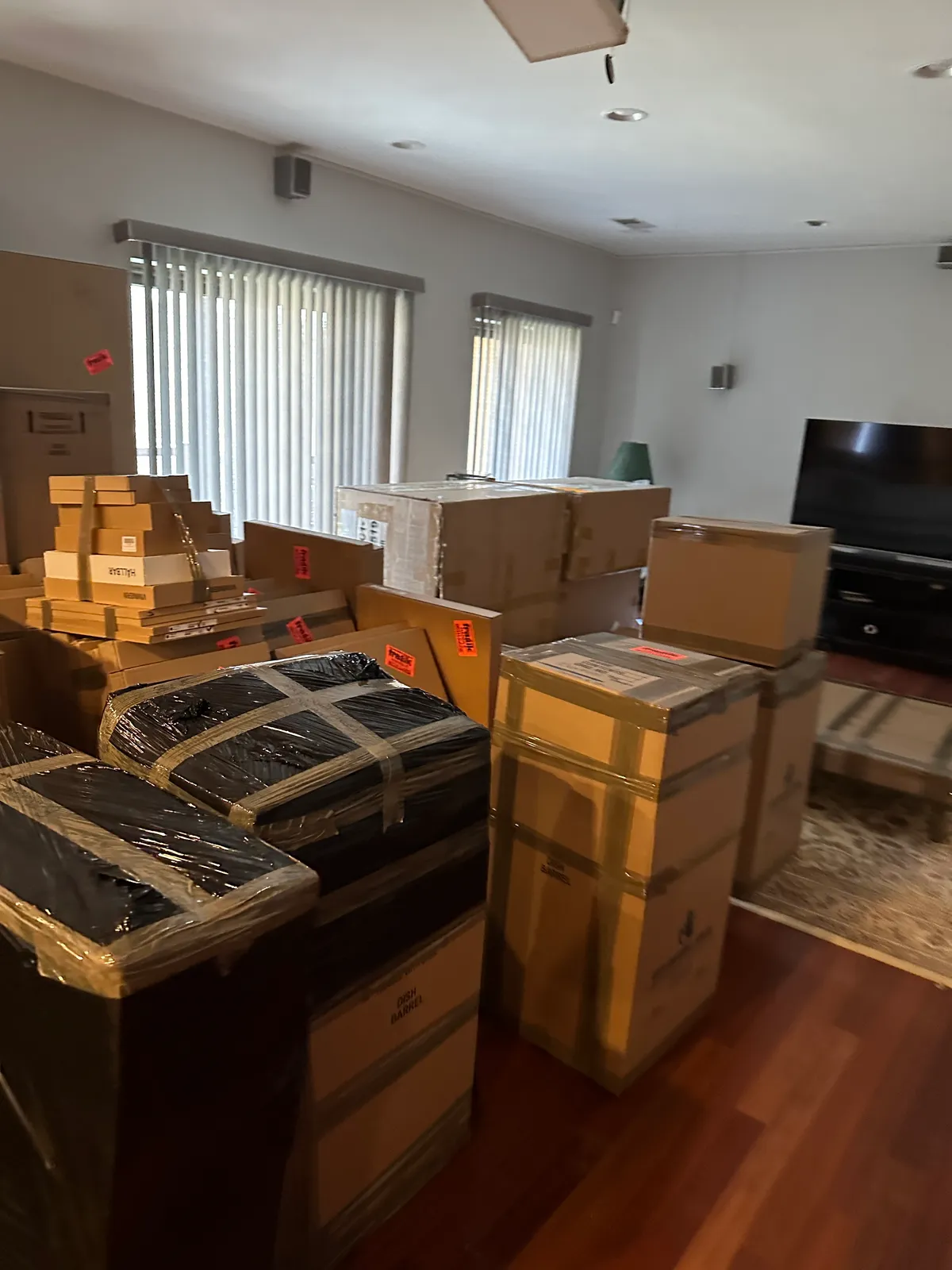 Living room filled with packed moving boxes, dish barrels, and stretch-wrapped furniture ready for loading