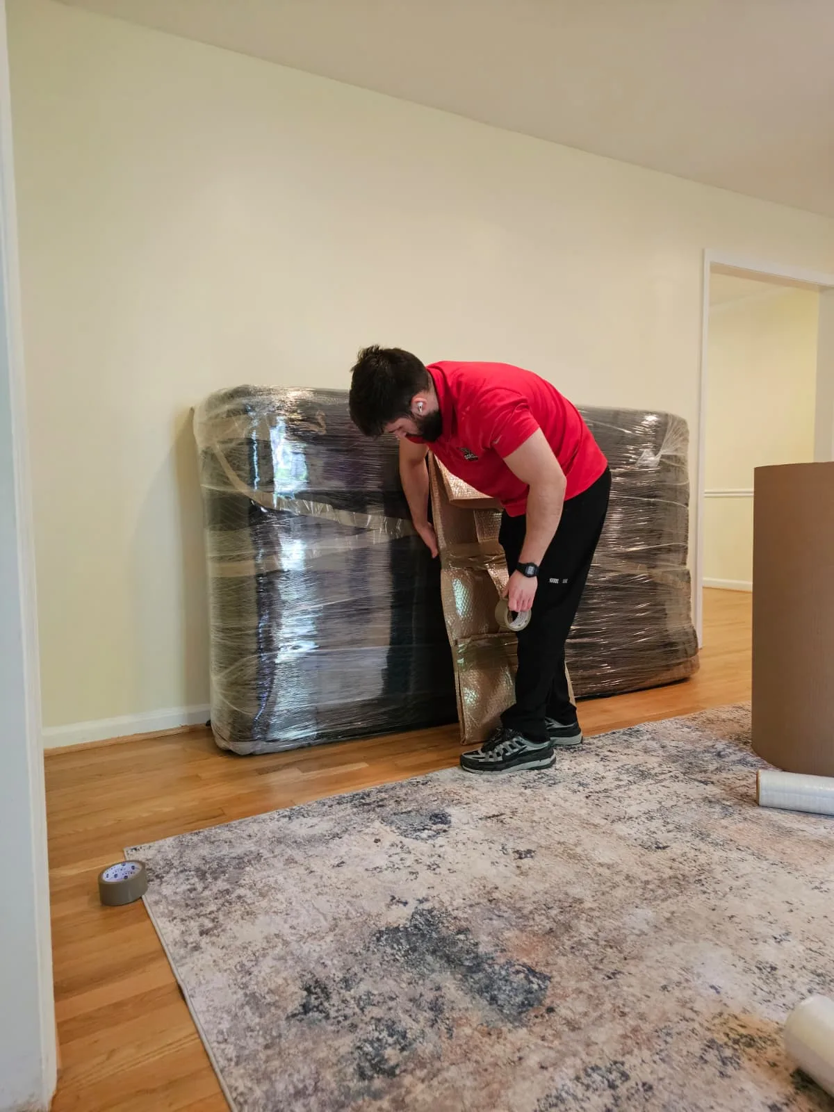 Gorilla Haulers mover taping cardboard protection around stretch-wrapped furniture