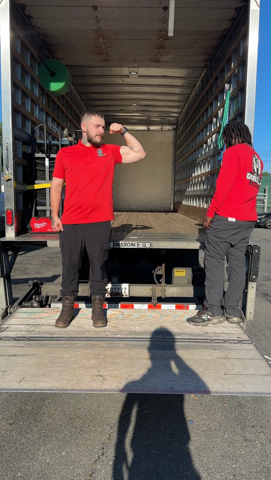 Two Gorilla Haulers movers on the liftgate of an empty moving truck, one flexing for the camera