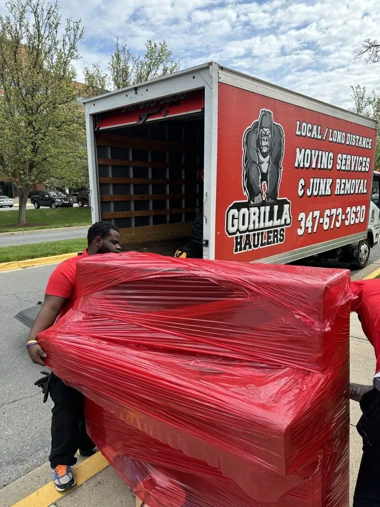 Gorilla Haulers crew carrying red-wrapped furniture beside a truck during junk removal