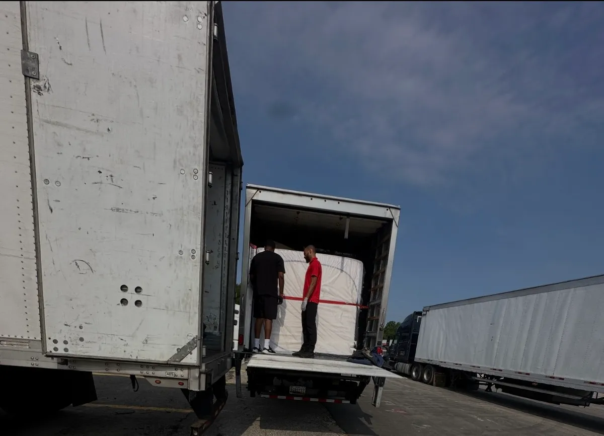 Gorilla Haulers movers loading a wrapped, strapped shipment into a moving truck beside a semi-trailer