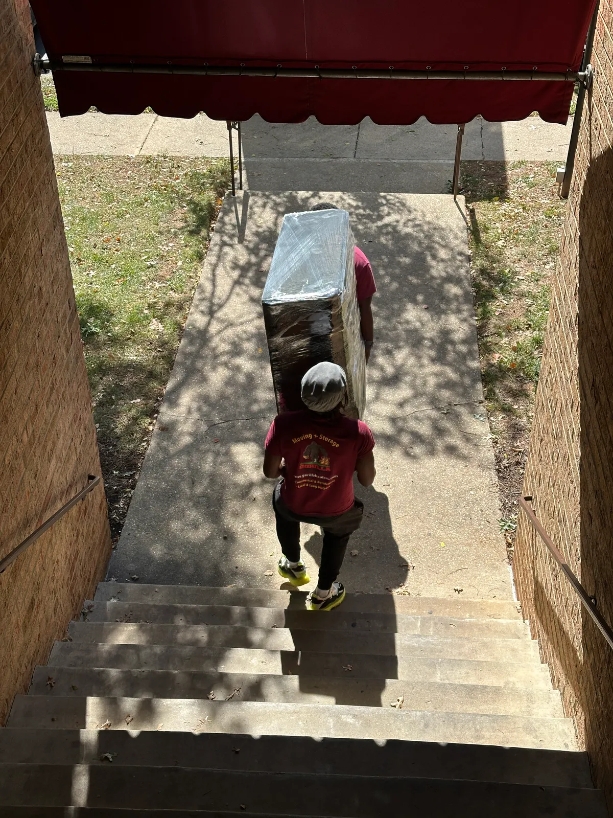 Two Gorilla Haulers movers carrying a stretch-wrapped dresser down outdoor brick stairs