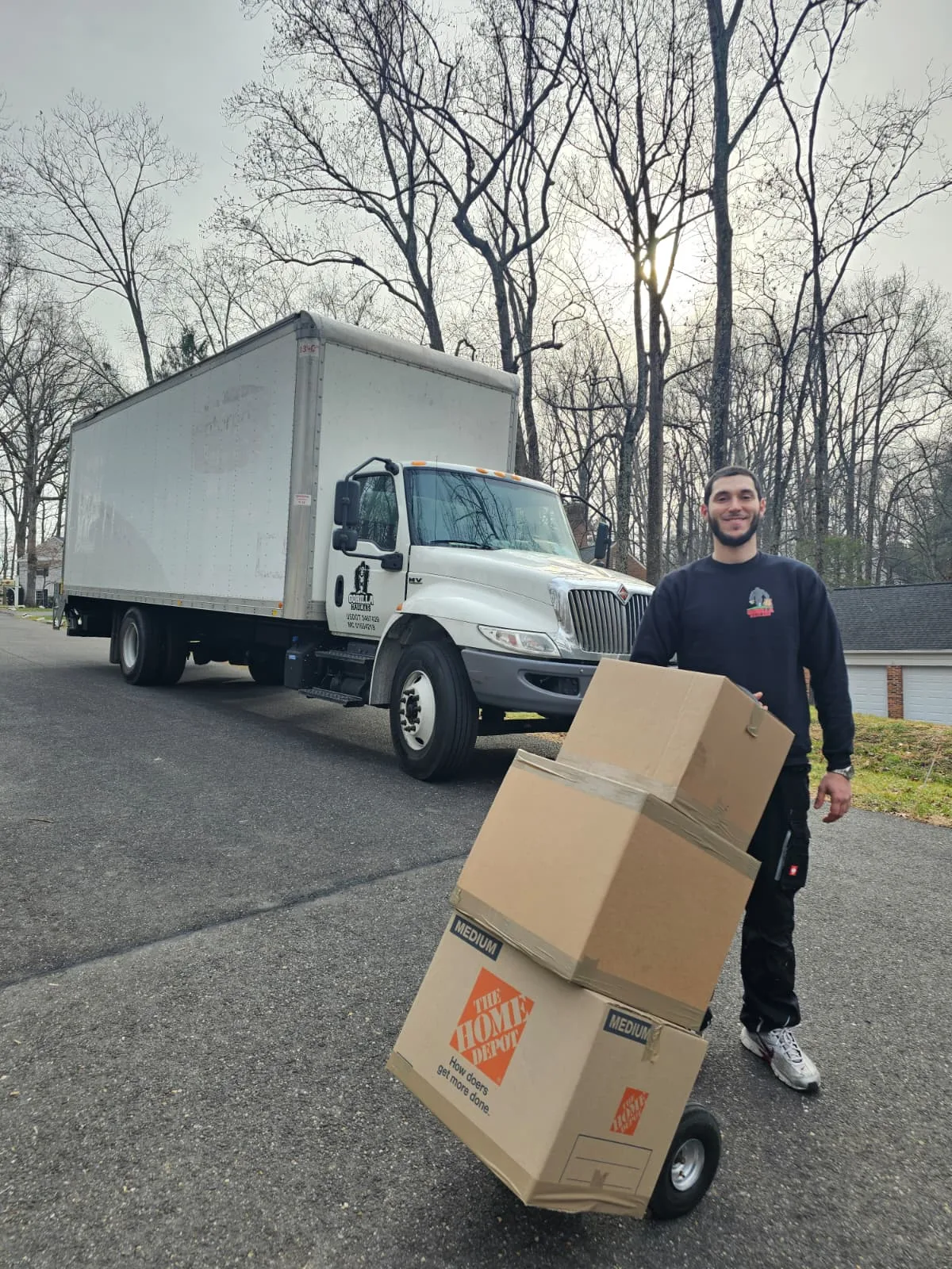 Gorilla Haulers mover transporting stacked moving boxes on a hand truck beside a company moving truck