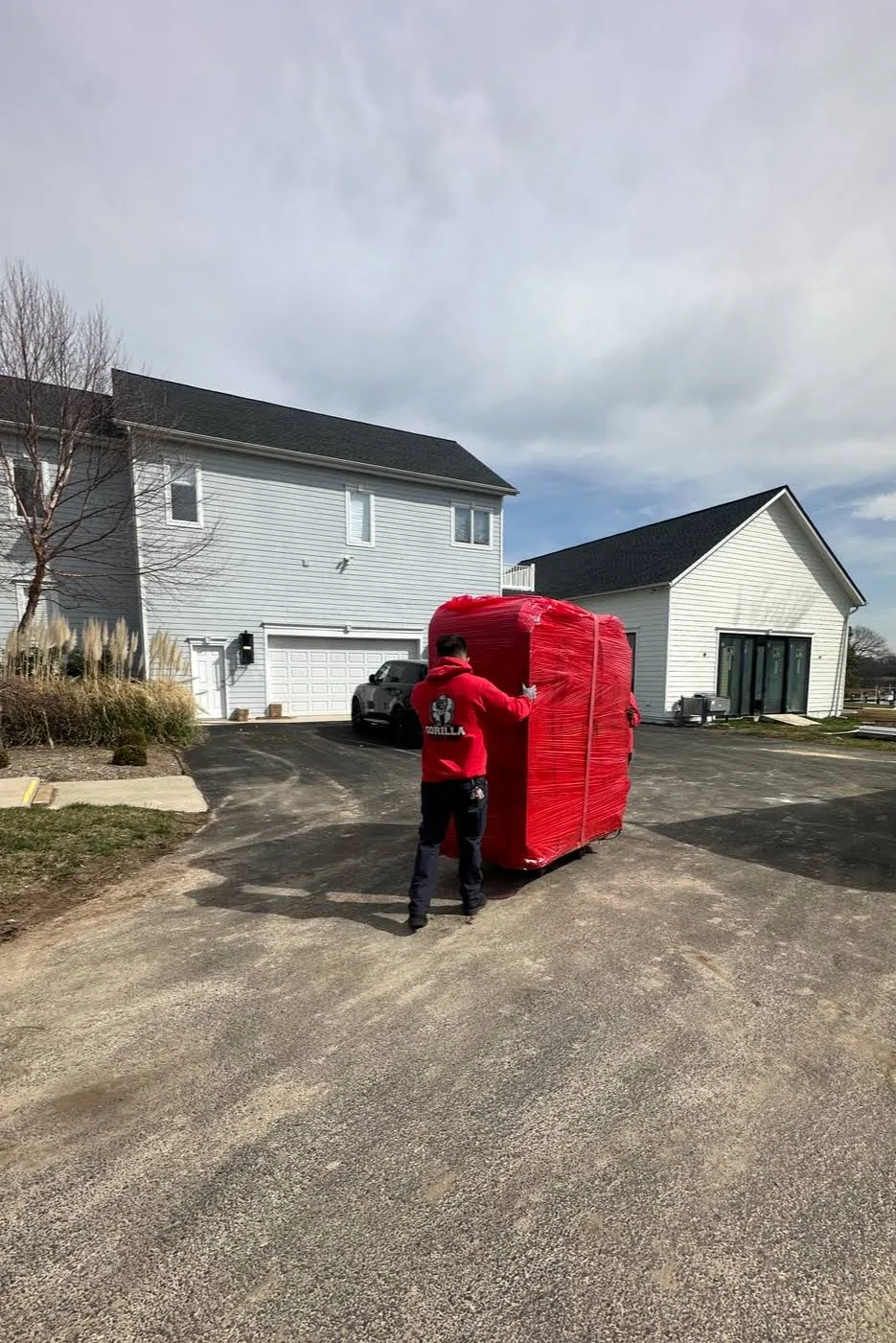 Gorilla Haulers mover guiding a hot tub covered in red protective wrap along a residential driveway