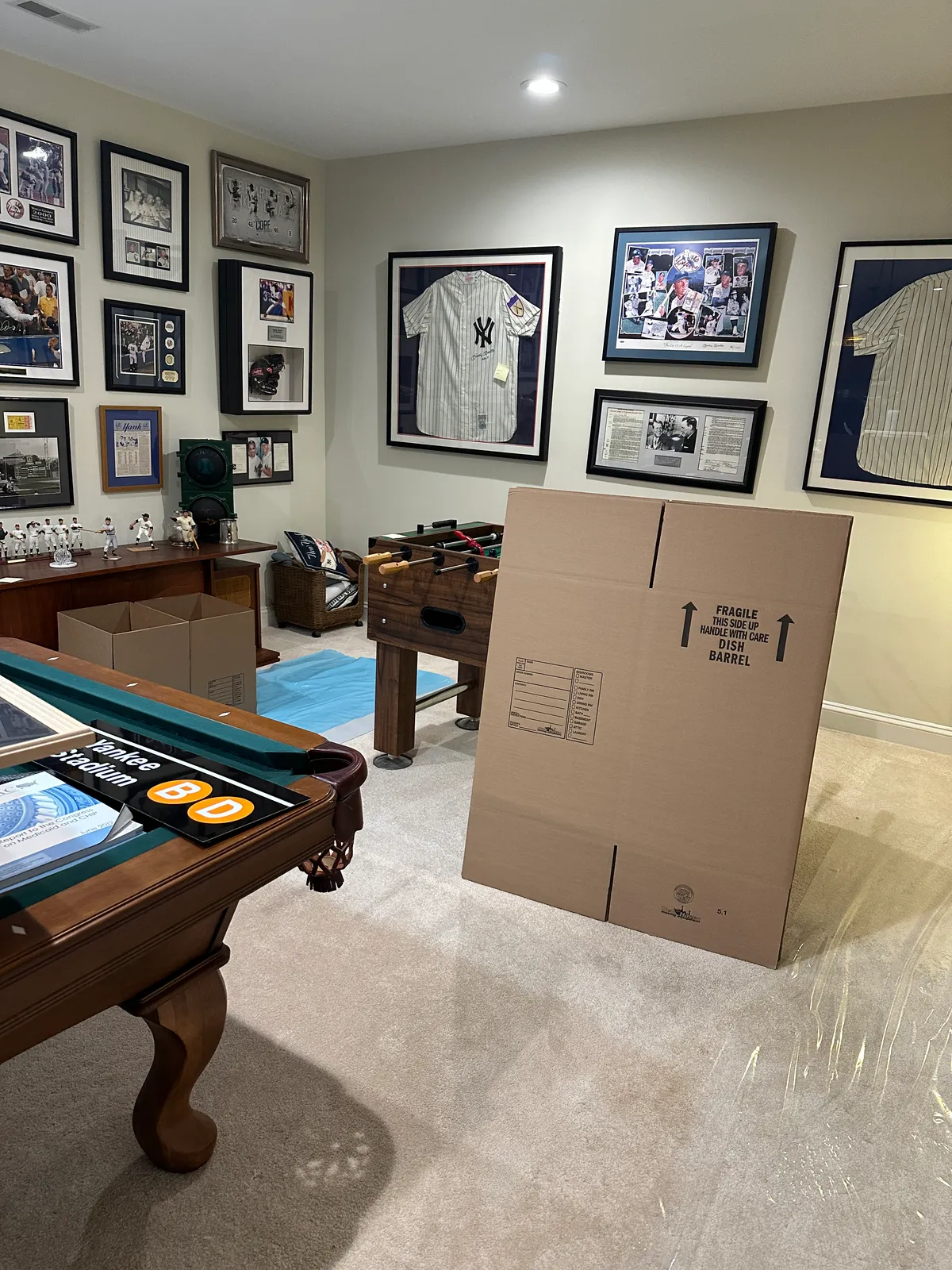 Game room filled with framed New York Yankees jerseys and memorabilia, a pool table, and floor protection film, ready for packing